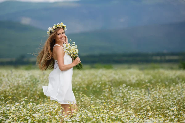 Hermosa joven en un campo de margaritas florecientes — Foto de Stock