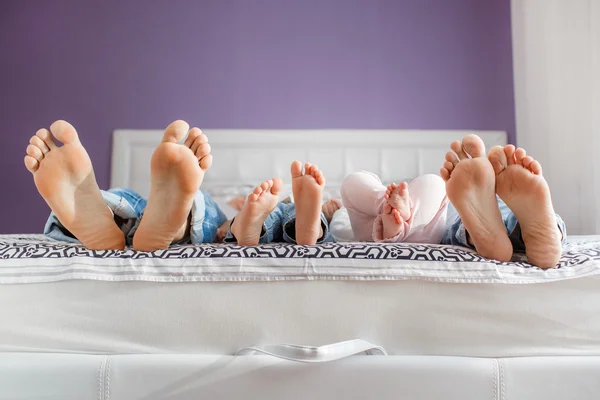 Pieds des parents et des enfants couchés sur le lit — Photo