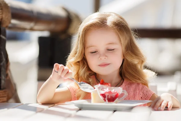 Little girl eating cake with strawberries in the summer cafe — ストック写真