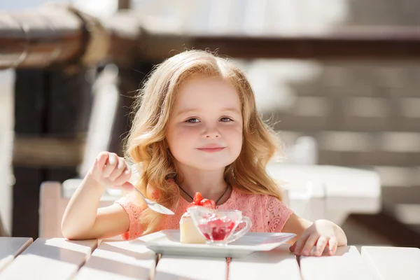 Little girl eating cake with strawberries in the summer cafe — Stok fotoğraf