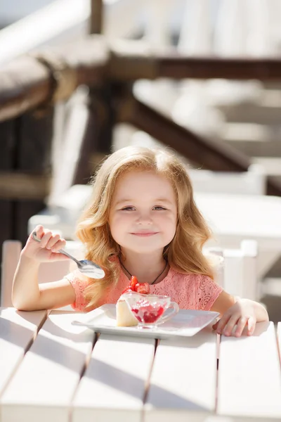 Niña comiendo pastel con fresas en el café de verano —  Fotos de Stock