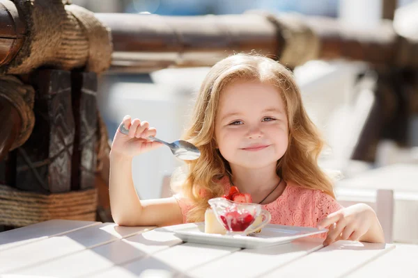 Little girl eating cake with strawberries in the summer cafe — Stockfoto