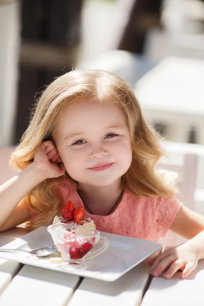 Little girl eating cake with strawberries in the summer cafe — Stockfoto