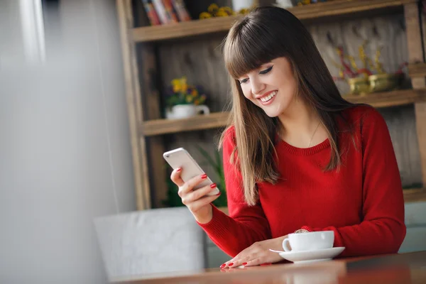 Chica leyendo SMS en el teléfono móvil sentado en la cafetería — Foto de Stock