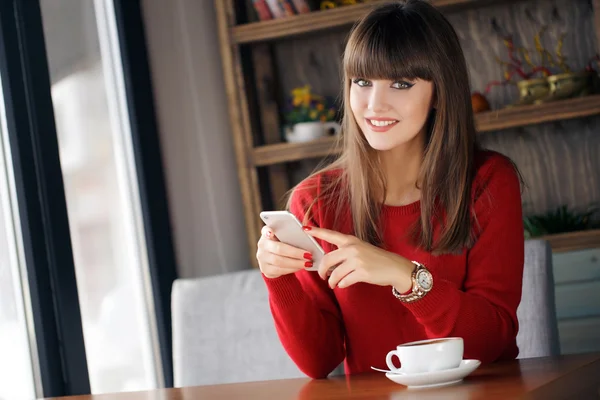 Chica leyendo SMS en el teléfono móvil sentado en la cafetería — Foto de Stock