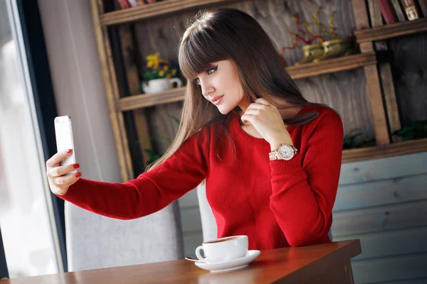 Chica leyendo SMS en el teléfono móvil sentado en la cafetería — Foto de Stock
