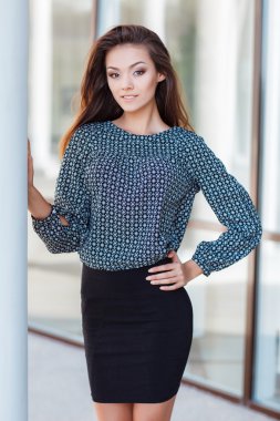 Portrait of a beautiful young woman standing near the glass building.