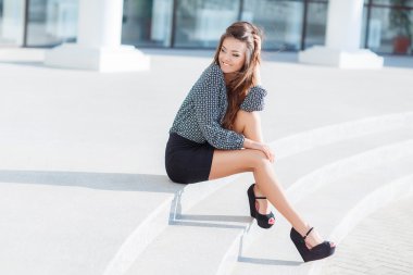 Portrait of a beautiful young woman, sitting on the stairs in the city.