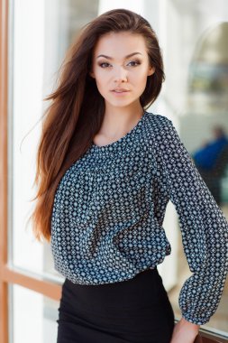 Portrait of a beautiful young woman standing near the glass building.