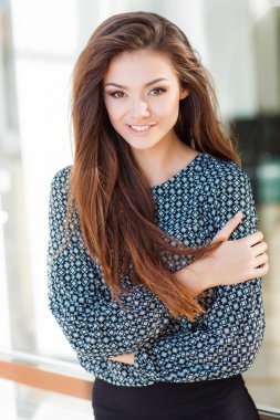 Portrait of a beautiful young woman standing near the glass building.
