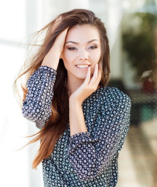 Portrait of a beautiful young woman standing near the glass building.