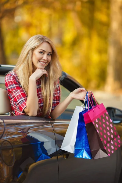 Joven mujer feliz con bolsas de compras en coche convertible al aire libre —  Fotos de Stock