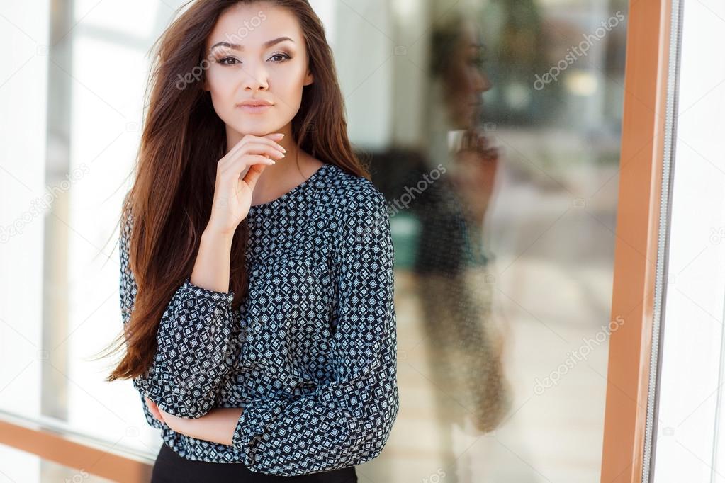 Portrait of a beautiful young woman standing near the glass building.