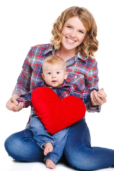 Feliz madre y su pequeño hijo sosteniendo una almohada en forma de corazones rojos . — Foto de Stock