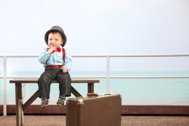 Bagaj ile oturan küçük şirin çocuk. Çocuklar seyahat kavramı