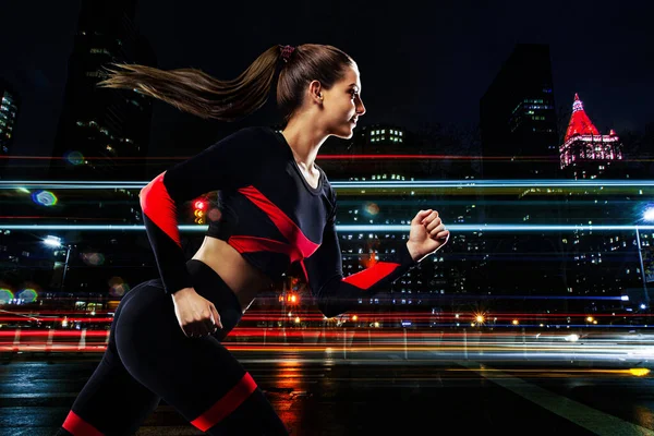 Fitness et motivation sportive. Forte athlète femme sprinteuse, courir dans la ville de nuit. Modèle fille en tenue de sport. Concept de coureur. — Photo