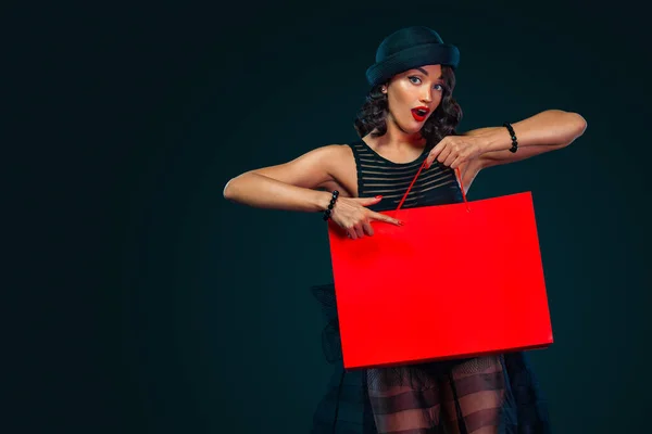Svart fredag försäljning koncept för butik. Shopping kvinna i klänning och hatt håller röd väska isolerad på mörk bakgrund — Stockfoto