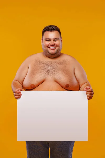 Hombre gordo y feliz sin camisa mostrando un anuncio de bandera blanca aislado sobre un fondo amarillo. — Foto de Stock