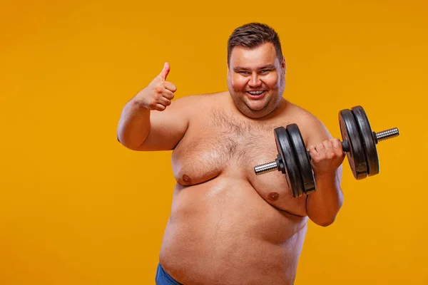 Hombre gordo haciendo ejercicio transpirando con pesas. Chico feliz aislado sobre fondo amarillo. —  Fotos de Stock