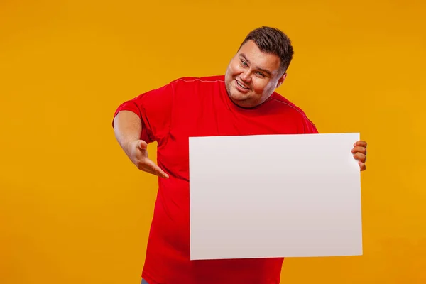 Kırmızı tişörtlü şişman adam sarı arka planda izole edilmiş beyaz pankart sergiliyor.. — Stok fotoğraf