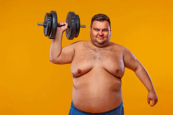 Hombre gordo haciendo ejercicio transpirando con pesas. Chico feliz aislado sobre fondo amarillo. —  Fotos de Stock