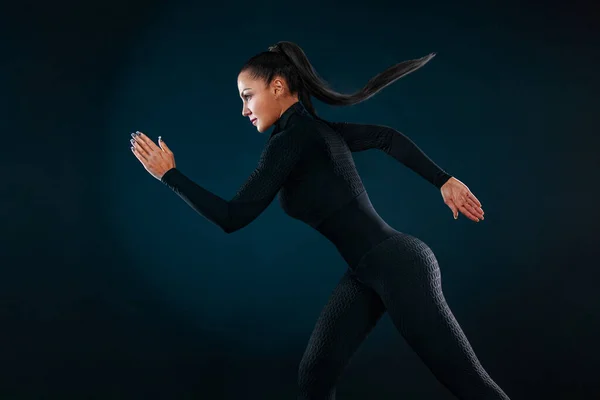 Fuerte atlético mujer velocista, corriendo sobre fondo negro que lleva en la ropa deportiva y auriculares. Fitness y motivación deportiva. Concepto de corredor. — Foto de Stock