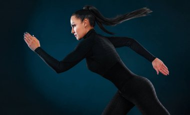 Güçlü atletik kadın koşucu, siyah arka planda koşuyor spor giyim ve kulaklık takıyor. Spor ve spor motivasyonu. Çalıştırıcı kavramı.
