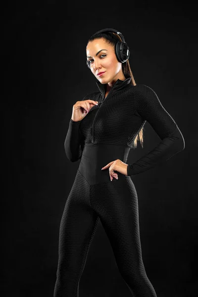 Sportkoncept. Sportig passform kvinna, idrottsman med hörlurar gör fitness övningar på svart bakgrund. — Stockfoto