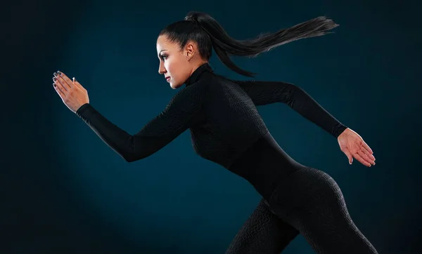 Sterke atletische vrouw sprinter, draait op zwarte achtergrond dragen in de sportkleding en hoofdtelefoon. Fitness en sport motivatie. Loopbaanconcept. — Stockfoto