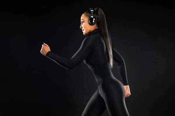 Fuerte atlético mujer velocista, corriendo sobre fondo negro que lleva en la ropa deportiva y auriculares. Fitness y motivación deportiva. Concepto de corredor. — Foto de Stock