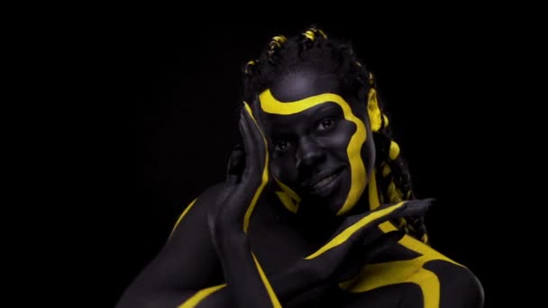 Yüz sanatı. Siyah ve sarı vücut boyalı dansçı kadın. Renkli vücut boyalı Afrikalı genç bir kız. Sarı makyajlı harika bir Afro-Amerikan modeli. Yakından bak.. — Stok video