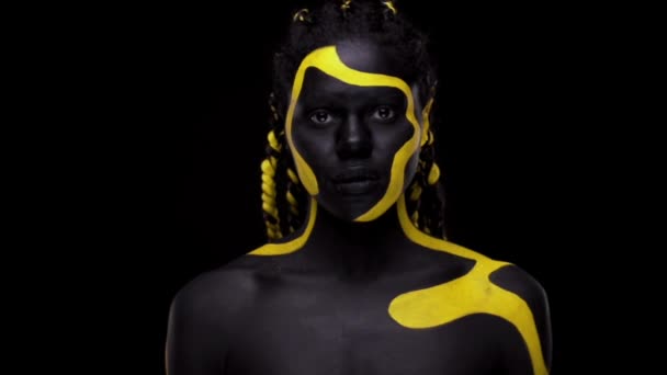 Cara de arte. Mujer bailarina con pintura corporal negra y amarilla. Chica africana joven con colorido bodypaint. Un increíble modelo afro-americano con maquillaje amarillo. Cara de primer plano. — Vídeo de stock