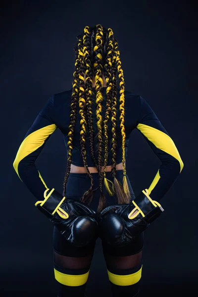 Concetto di pugilato sportivo. Donna con trecce gialle su sfondo nero. Ragazza sportivo muay thai pugile combattimento in guanti in palestra. — Foto Stock