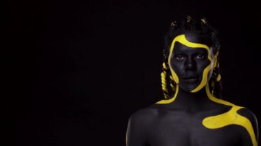 Yüz sanatı. Kopya boşluğunu parmaklarıyla gösteren bir kız. Siyah ve sarı vücut boyalı bir kadın. Renkli vücut boyalı Afrikalı genç bir kız. Makyajlı harika bir Afro-Amerikan modeli..