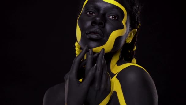 Искусство лица. Танцующая женщина с черно-желтой краской для тела. Молодая африканская девушка с красочной бодикраской. Удивительная афро-американская модель с желтым макияжем. Крупный план. — стоковое видео
