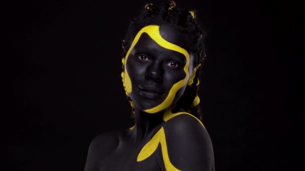 Cara de arte. Mujer con pintura corporal negra y amarilla. Chica africana joven con colorido bodypaint. Un increíble modelo afro-americano con maquillaje amarillo. — Vídeo de stock