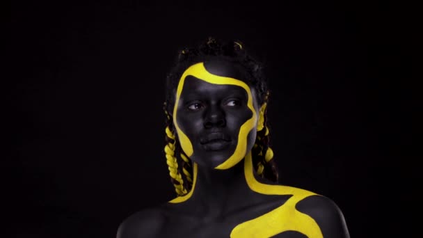 Cara de arte. Mujer con pintura corporal negra y amarilla. Chica africana joven con colorido bodypaint. Un increíble modelo afro-americano con maquillaje amarillo. — Vídeo de stock