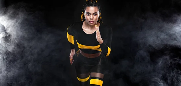 Forte athlète femme sprinteuse, courant sur fond noir vêtue de vêtements de sport. Fitness et motivation sportive. Concept de coureur. — Photo