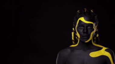 Yüz sanatı. Parmaklarıyla işaret veren bir kız. Siyah ve sarı vücut boyalı bir kadın. Renkli vücut boyalı Afrikalı genç bir kız. Makyajlı harika bir Afro-Amerikan modeli..