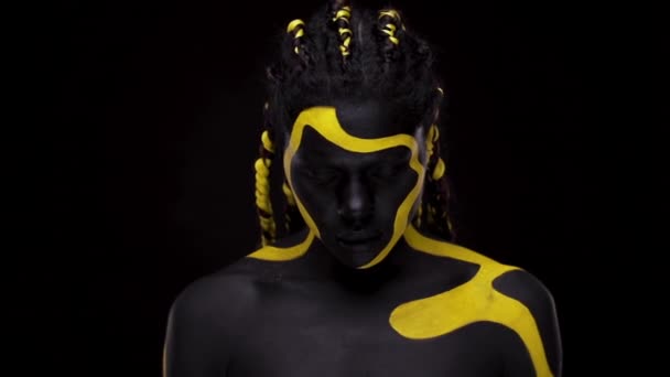 Face art. Femme dansante avec peinture pour le corps noir et jaune. Jeune fille africaine avec peinture colorée du corps. Un modèle afro-américain étonnant avec un maquillage jaune. Gros plan sur le visage. — Video