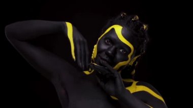 Yüz sanatı. Siyah ve sarı vücut boyalı dansçı kadın. Renkli vücut boyalı Afrikalı genç bir kız. Sarı makyajlı harika bir Afro-Amerikan modeli. Yakından bak..