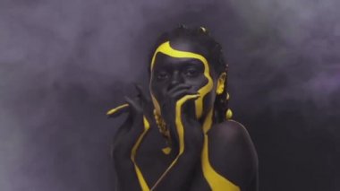 Yüz sanatı. Siyah ve sarı vücut boyalı bir kadın. Renkli vücut boyalı Afrikalı genç bir kız. Sarı makyajlı harika bir Afro-Amerikan modeli..