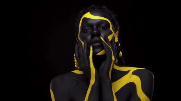 Ansiktskonst. Dansande kvinna med svart och gul kroppsfärg. Ung afrikansk flicka med färgglad kroppsfärg. En fantastisk afro amerikansk modell med gul makeup. Närbild ansikte. — Stockvideo