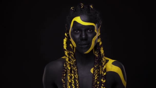 Cara de arte. Mujer con pintura corporal negra y amarilla. Chica africana joven con colorido bodypaint. Un increíble modelo afro-americano con maquillaje amarillo. — Vídeo de stock