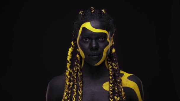 Gesichtskunst. Schreiend knurrende wilde Frau mit schwarz-gelber Körperfarbe. Junges afrikanisches Mädchen mit farbenfroher Bodypaint. Ein erstaunliches afroamerikanisches Model mit gelbem Make-up. — Stockvideo