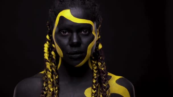 Ansiktskonst. Kvinna med svart och gul kroppsfärg. Ung afrikansk flicka med färgglad kroppsfärg. En fantastisk afro amerikansk modell med gul makeup. — Stockvideo