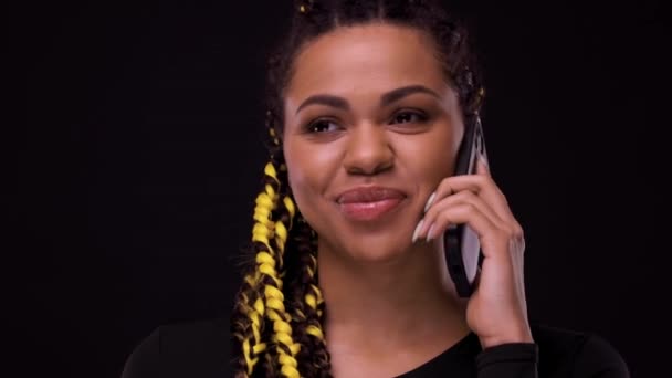 Portret van een lachend Afrikaans meisje dat met een mobiele telefoon praat. vrouw geïsoleerd over zwarte achtergrond — Stockvideo