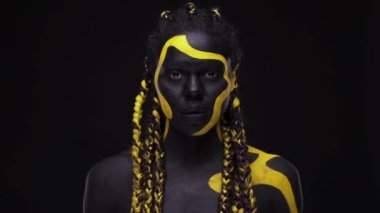 Yüz sanatı. Siyah ve sarı vücut boyalı, hırıltılı vahşi bir kadın. Renkli vücut boyalı Afrikalı genç bir kız. Sarı makyajlı harika bir Afro-Amerikan modeli..