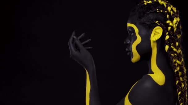 Face art. Femeie cu vopsea neagră şi galbenă. O tânără africană cu vopsea colorată. Un model afro-american uimitor cu machiaj galben . — Videoclip de stoc