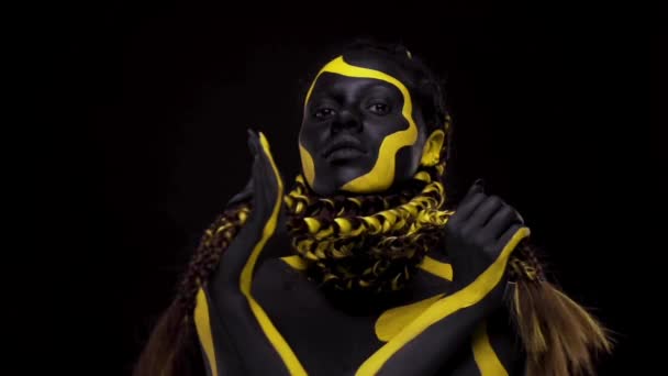 Face art. Femme dansante avec peinture pour le corps noir et jaune. Jeune fille africaine avec peinture colorée du corps. Un modèle afro-américain étonnant avec un maquillage jaune. Gros plan sur le visage. — Video